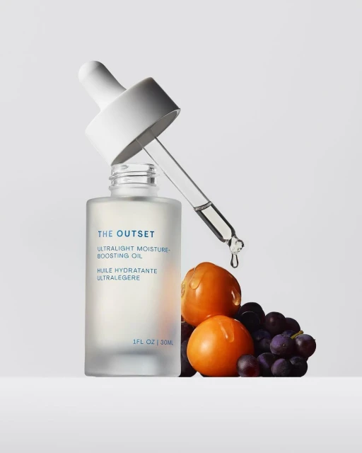 Cosmetic oil in a frosted glass bottle with dropper, featuring grapes and golden berries on a white background for beauty photography.