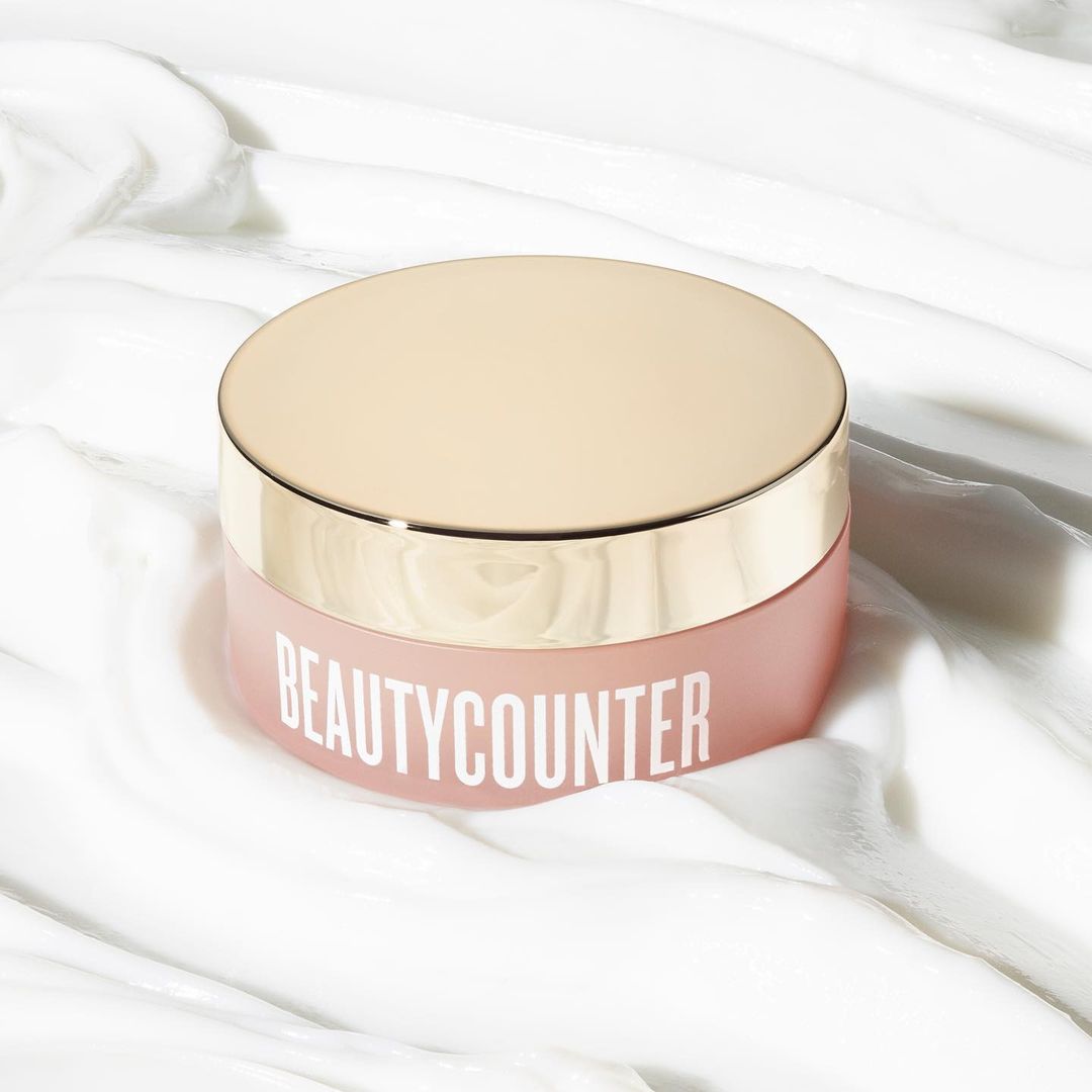 Product shot of a jar of Beautycounter skincare on a white, textured surface. The jar has a rose-colored body and gold lid.