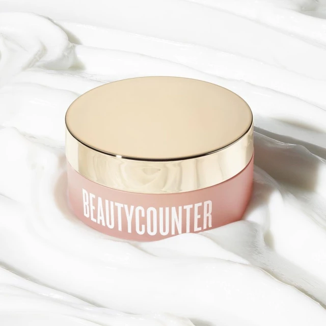 Product shot of a jar of Beautycounter skincare on a white, textured surface. The jar has a rose-colored body and gold lid.