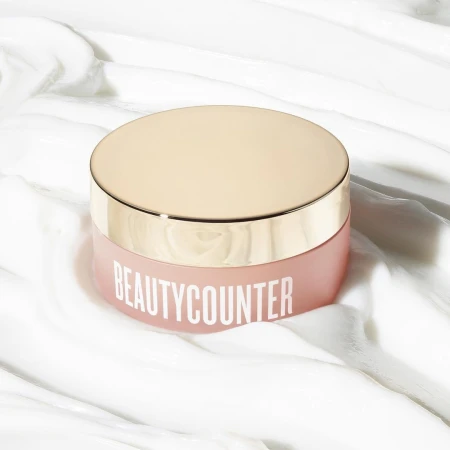 Product shot of a jar of Beautycounter skincare on a white, textured surface. The jar has a rose-colored body and gold lid.