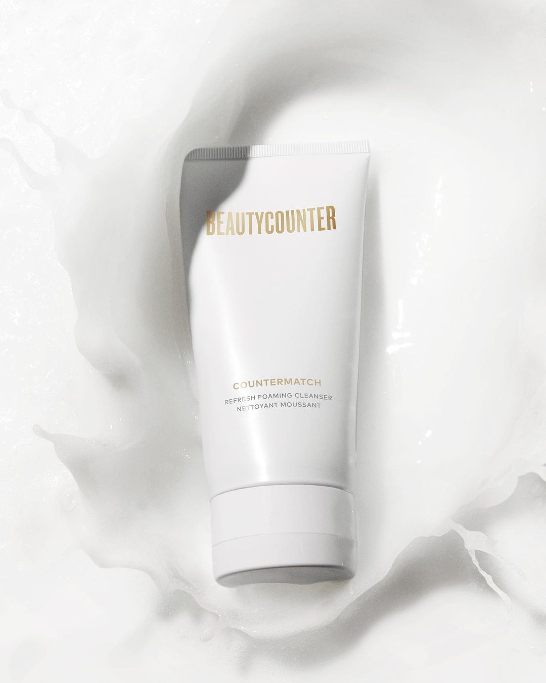 BeautyCounter product in white tube surrounded by white cream on a white background, showcasing a clean and minimalist aesthetic.