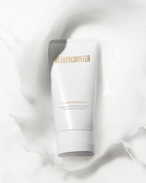 BeautyCounter product in white tube surrounded by white cream on a white background, showcasing a clean and minimalist aesthetic.
