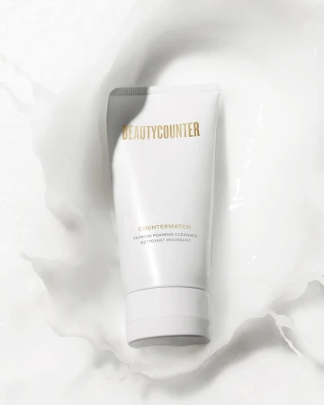 BeautyCounter product in white tube surrounded by white cream on a white background, showcasing a clean and minimalist aesthetic.