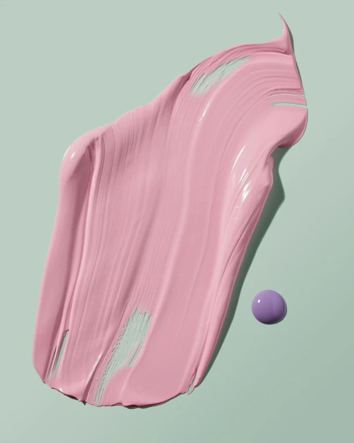 Close-up of a swipe of pink paint or cosmetic cream with a small purple sphere, against a light green background, studio lighting.