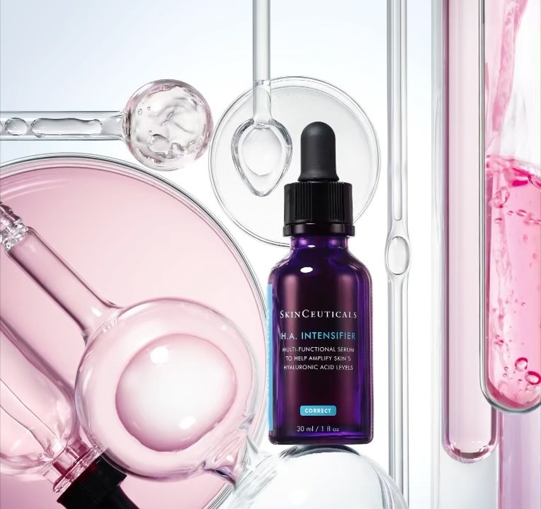 Skinceuticals H.A. Intensifier bottle surrounded by clear glass lab equipment and pink liquid in a bright, product-focused studio shot.