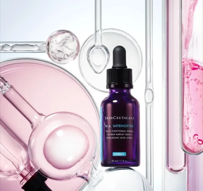 Skinceuticals H.A. Intensifier bottle surrounded by clear glass lab equipment and pink liquid in a bright, product-focused studio shot.