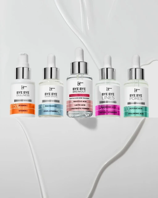 Five bottles of IT Cosmetics Bye Bye serums sit on a white surface, each targeting different skin concerns, like dullness, dark spots, and pores.