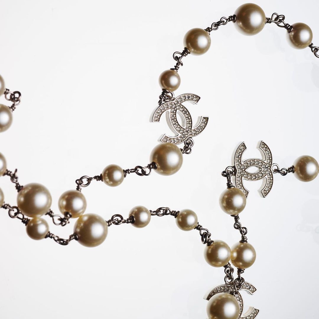 Elegant pearl necklace featuring the Chanel logo on a light background, showcasing a classic fashion accessory.