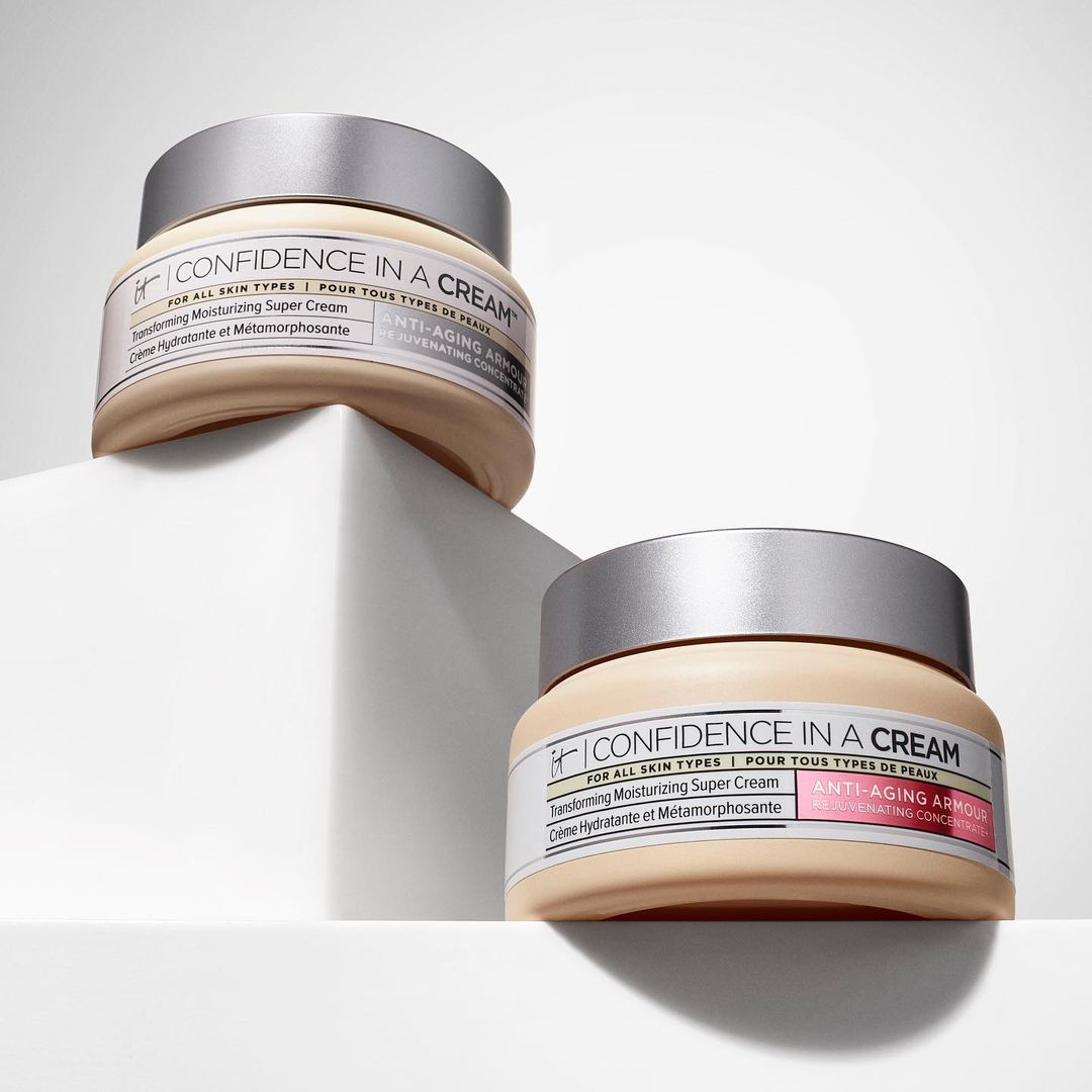 Two jars of 'Confidence in a Cream' skincare product are displayed on a white geometric platform against a bright white background.