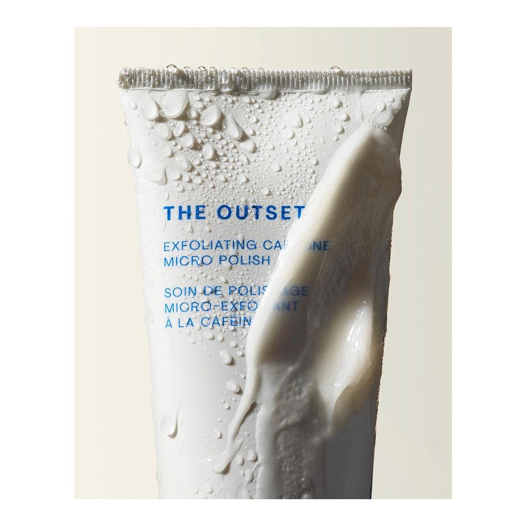 Cosmetic tube of 'The Outset' exfoliating caffeine micro polish with water droplets and a blob of cream, studio shot.