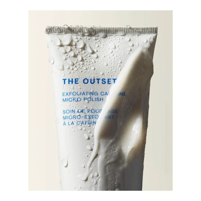 Cosmetic tube of 'The Outset' exfoliating caffeine micro polish with water droplets and a blob of cream, studio shot.