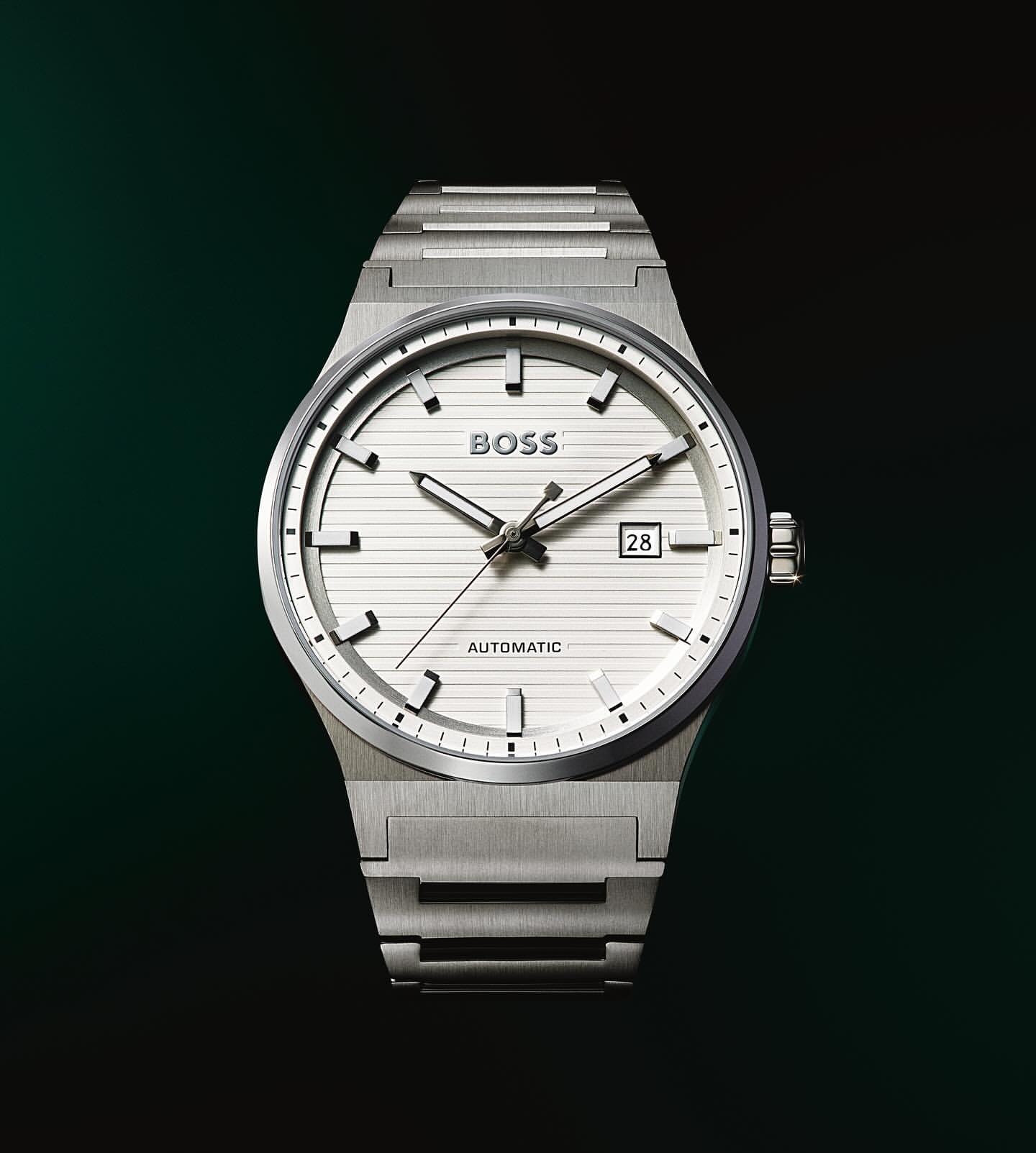 Silver-toned automatic wristwatch with a white face and date window against a dark green background, highlighting its sophisticated design.