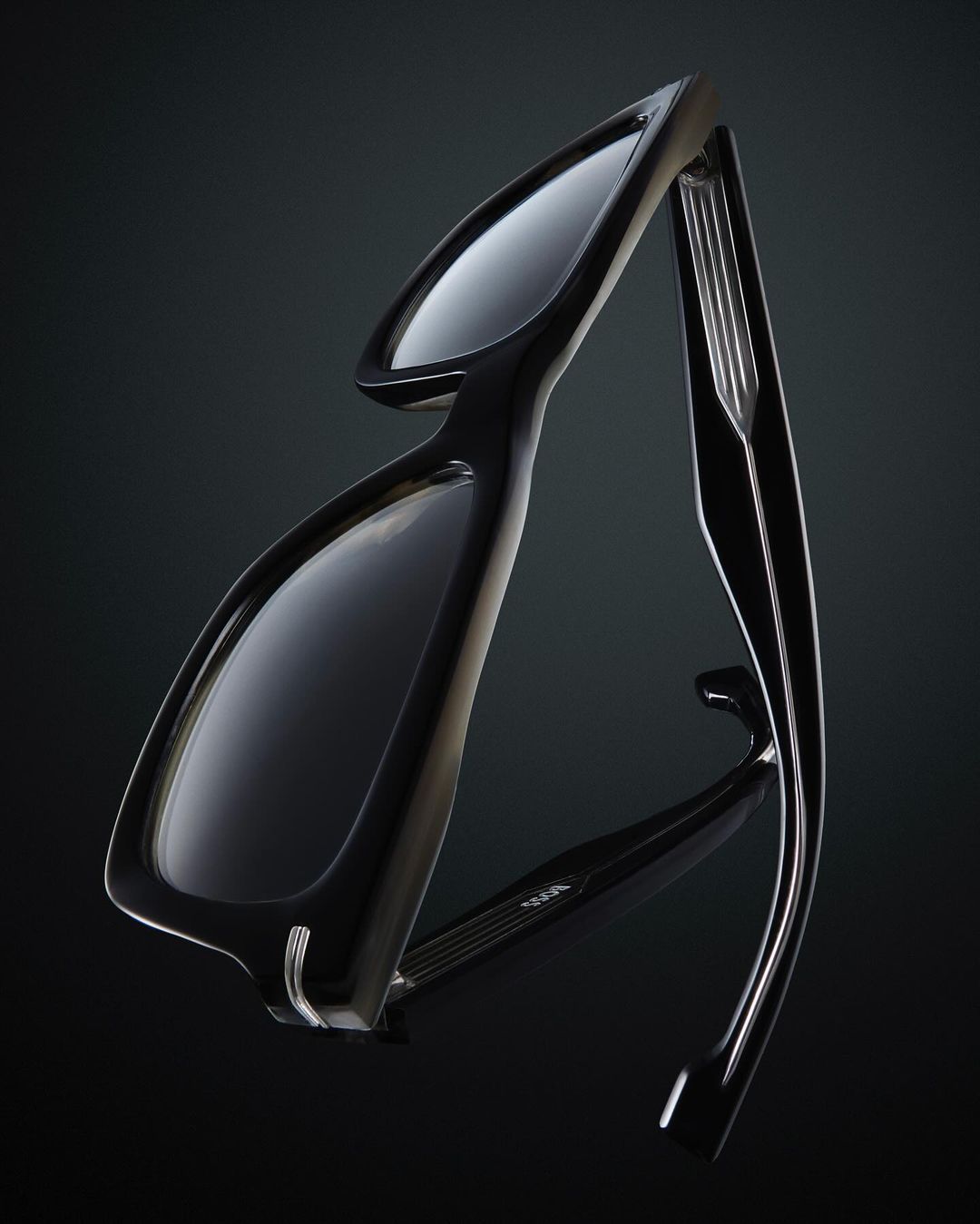 Close-up studio shot of sleek black eyeglasses with a reflective surface against a dark background, emphasizing the design and materials.