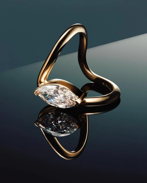 Close-up studio shot of a gold ring featuring a large, clear marquise-cut diamond, reflected on a glossy dark surface.