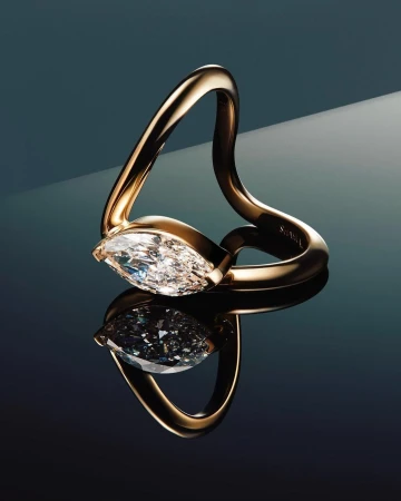 Close-up studio shot of a gold ring featuring a large, clear marquise-cut diamond, reflected on a glossy dark surface.