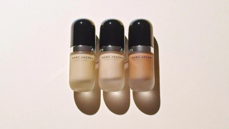 Three Marc Jacobs cosmetics bottles with rounded black caps and frosted glass standing upright in a row on a light surface.