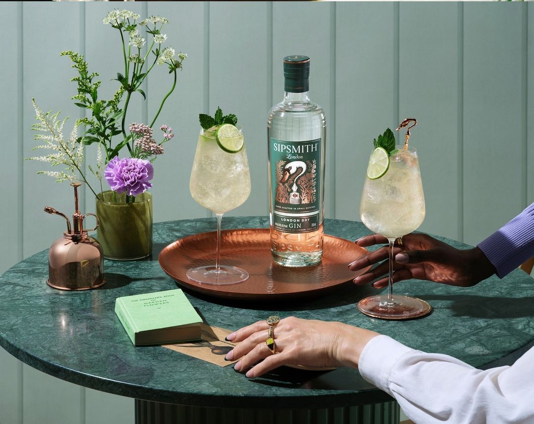 Sipsmith gin bottle and cocktails on a marble table, presented by two people and decorated with flowers, showcasing an elegant presentation.