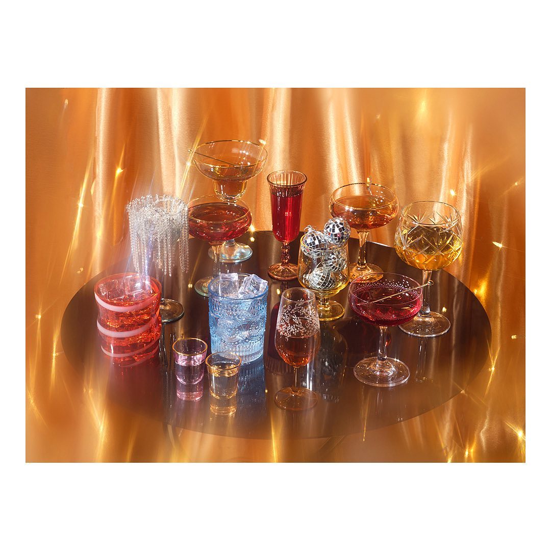 Elevated shot of diverse cocktail glasses with colorful liquids on a reflective surface against a shimmering gold backdrop, studio lighting.