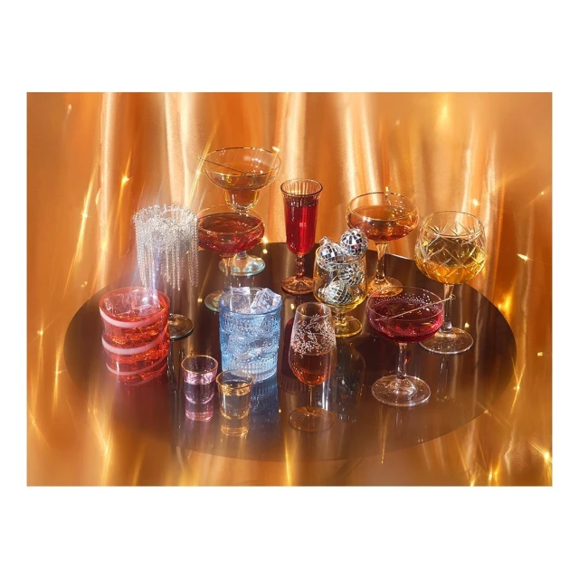 Elevated shot of diverse cocktail glasses with colorful liquids on a reflective surface against a shimmering gold backdrop, studio lighting.
