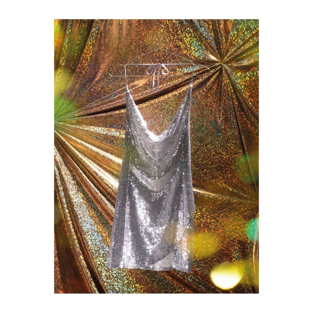 Silver sequin halter top dress hanging against a gold abstract background in a studio shot, fashion advertisement.