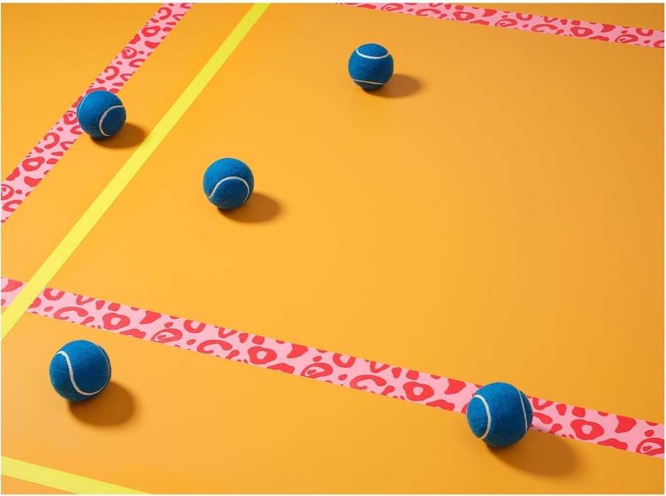 Five tennis balls are arranged on an orange surface with patterned decorative tape, creating an abstract, visually appealing composition.