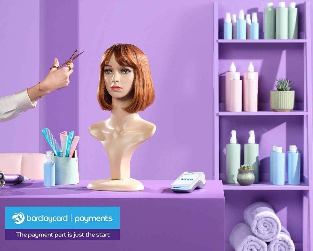 Mannequin head with bob wig being styled, surrounded by salon tools, against a purple background with Barclaycard logo.