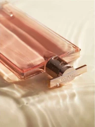 Close-up of a Lancome perfume bottle resting on rippling golden liquid surface with water droplets.