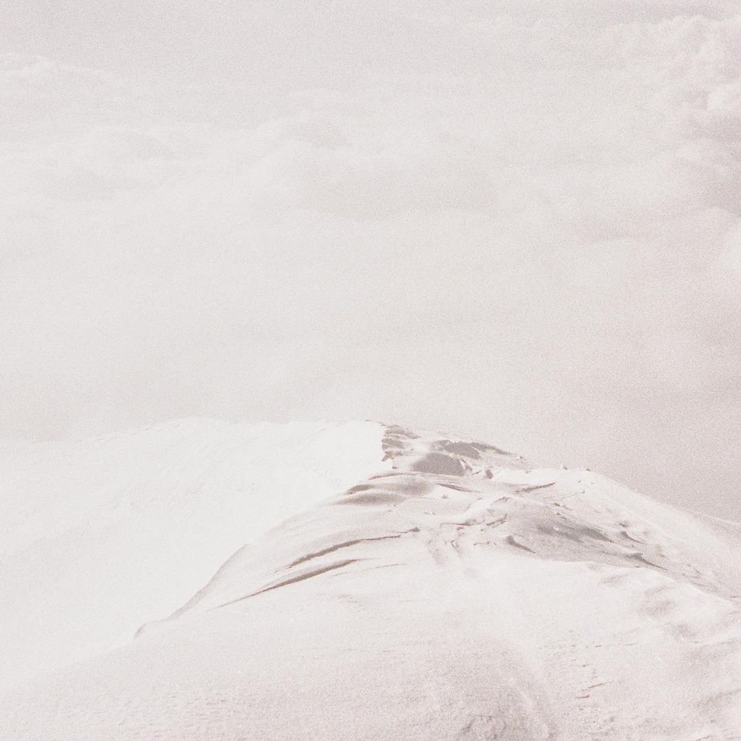 Snow-covered mountain peak against a cloudy sky. Soft, diffused light creates a serene and minimalist landscape. Winter nature scene.
