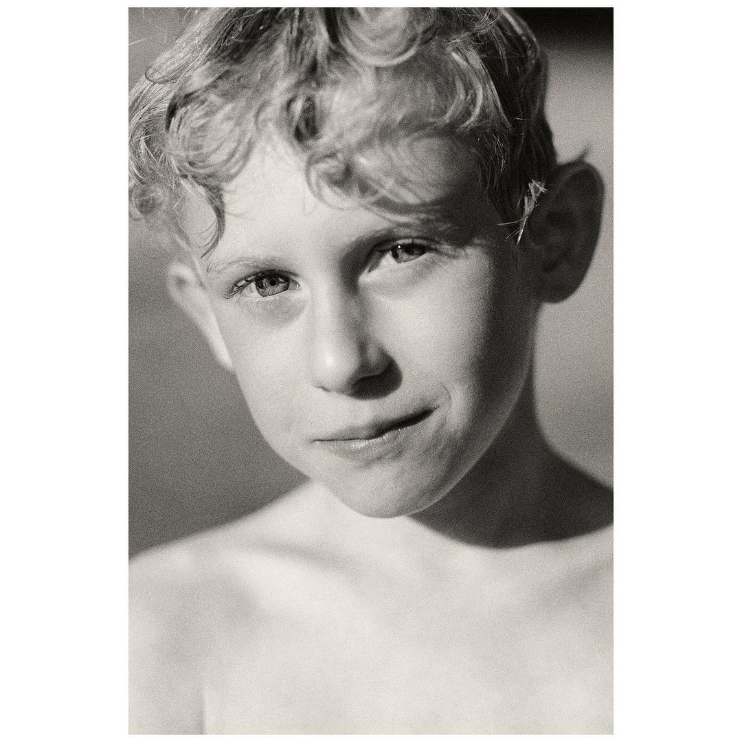 Close-up portrait of a young fair-skinned child with curly blond hair, looking directly at the camera with a slight smile in a monochrome photograph.