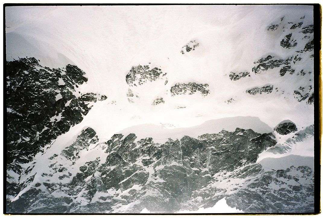 Snow-covered mountain landscape featuring a blend of white snow, grey rocks, and dynamic textures, captured in a high-angle scenic view.