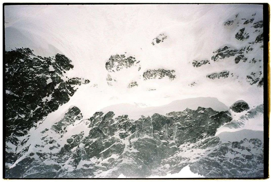 Snow-covered mountain landscape featuring a blend of white snow, grey rocks, and dynamic textures, captured in a high-angle scenic view.
