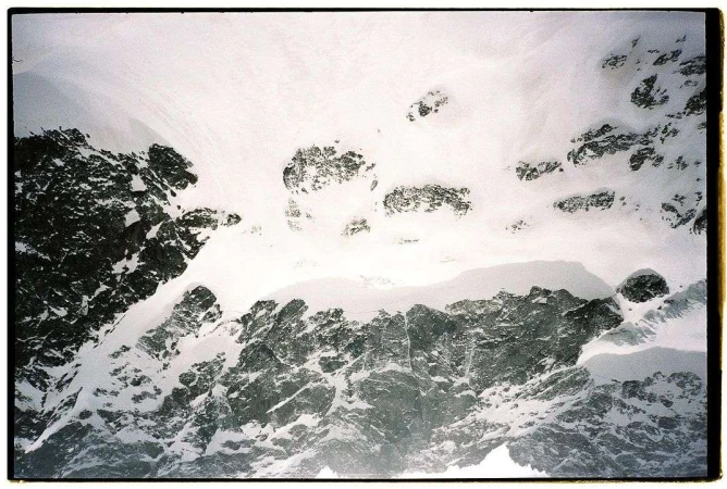 Snow-covered mountain landscape featuring a blend of white snow, grey rocks, and dynamic textures, captured in a high-angle scenic view.