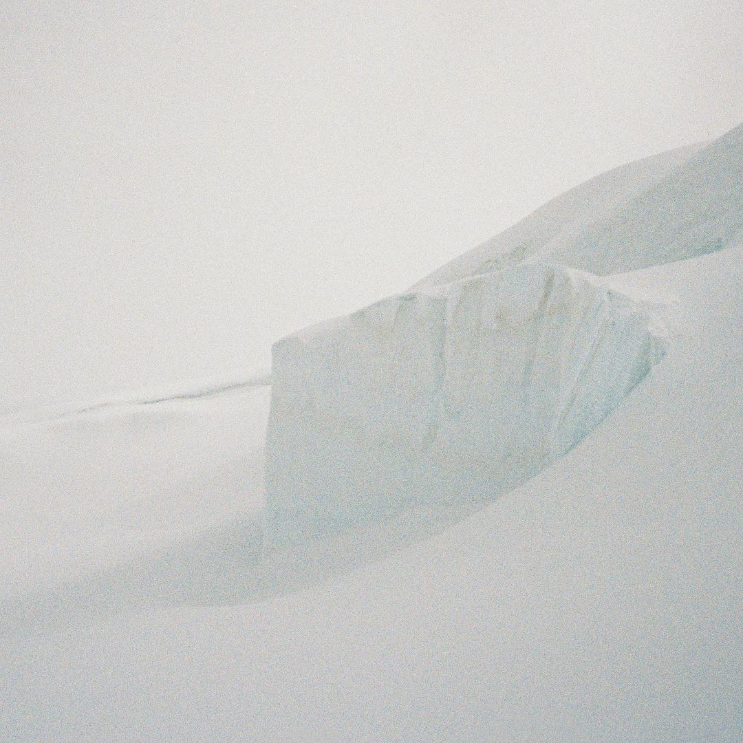 Icy landscape featuring a large chunk of glacier ice in the foreground, with snow-covered land receding into a hazy, overcast background.