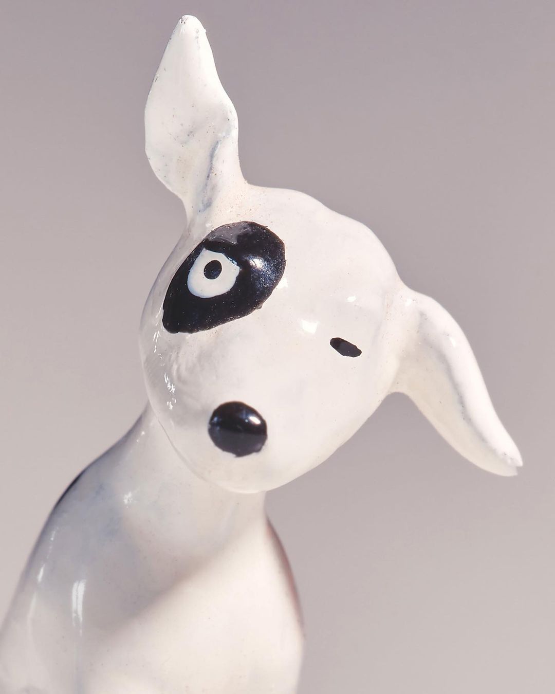 White bull terrier statuette with black markings displayed indoors on a solid background. The statuette is the primary focus.
