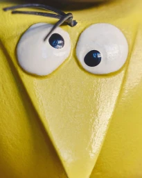 Extreme close-up of a bright yellow painted object featuring large white googly eyes with dark pupils and wire antennae.