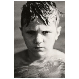 Close-up portrait of a young boy in water with wet hair, captured in grainy monochrome by Vincent Bousserez in Paris.