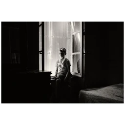 A young boy sitting in a window frame with bright light streaming through, photographed in black and white by Vincent Bousserez.