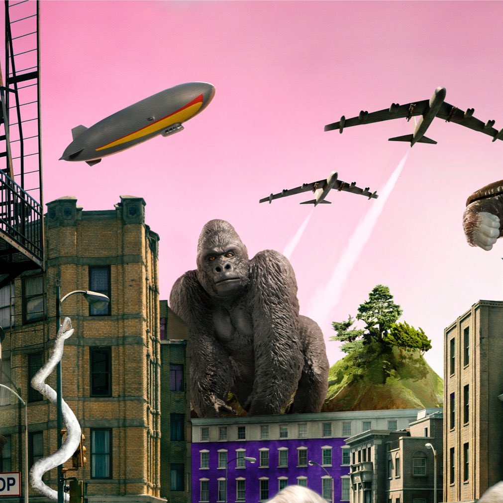 Surreal cityscape with a giant gorilla on a building, airplanes, and a blimp under a pink sky, blending urban and fantastical elements.
