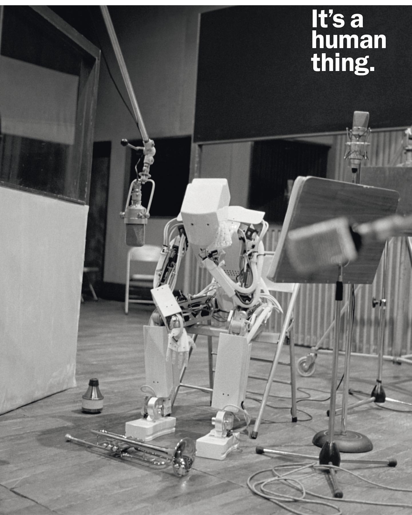 Monochrome shot of a humanoid robot seated in a recording studio, looking contemplative alongside musical instruments and equipment.