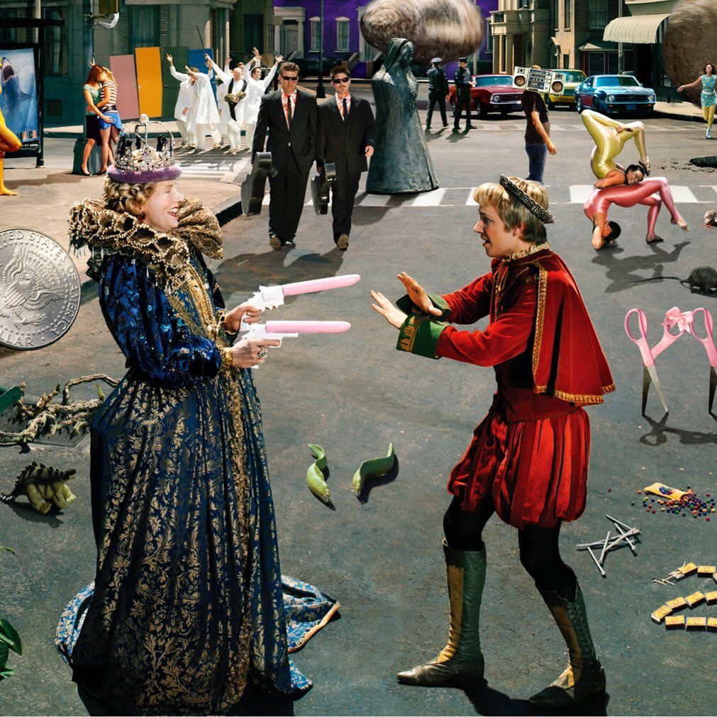 Two people in period costumes point toy guns at each other on a city street, with a crowd of people in the background.