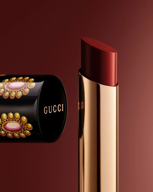 Gucci lipstick tube and open lipstick on a gradient maroon backdrop. The tube has decorative gold and pink floral accents.