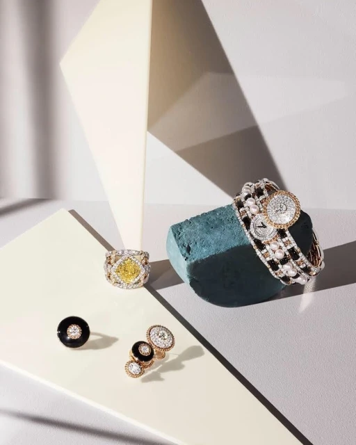 High-angle shot of gold and gemstone jewelry, including a bracelet, rings, and earrings, arranged against a modern geometric backdrop.