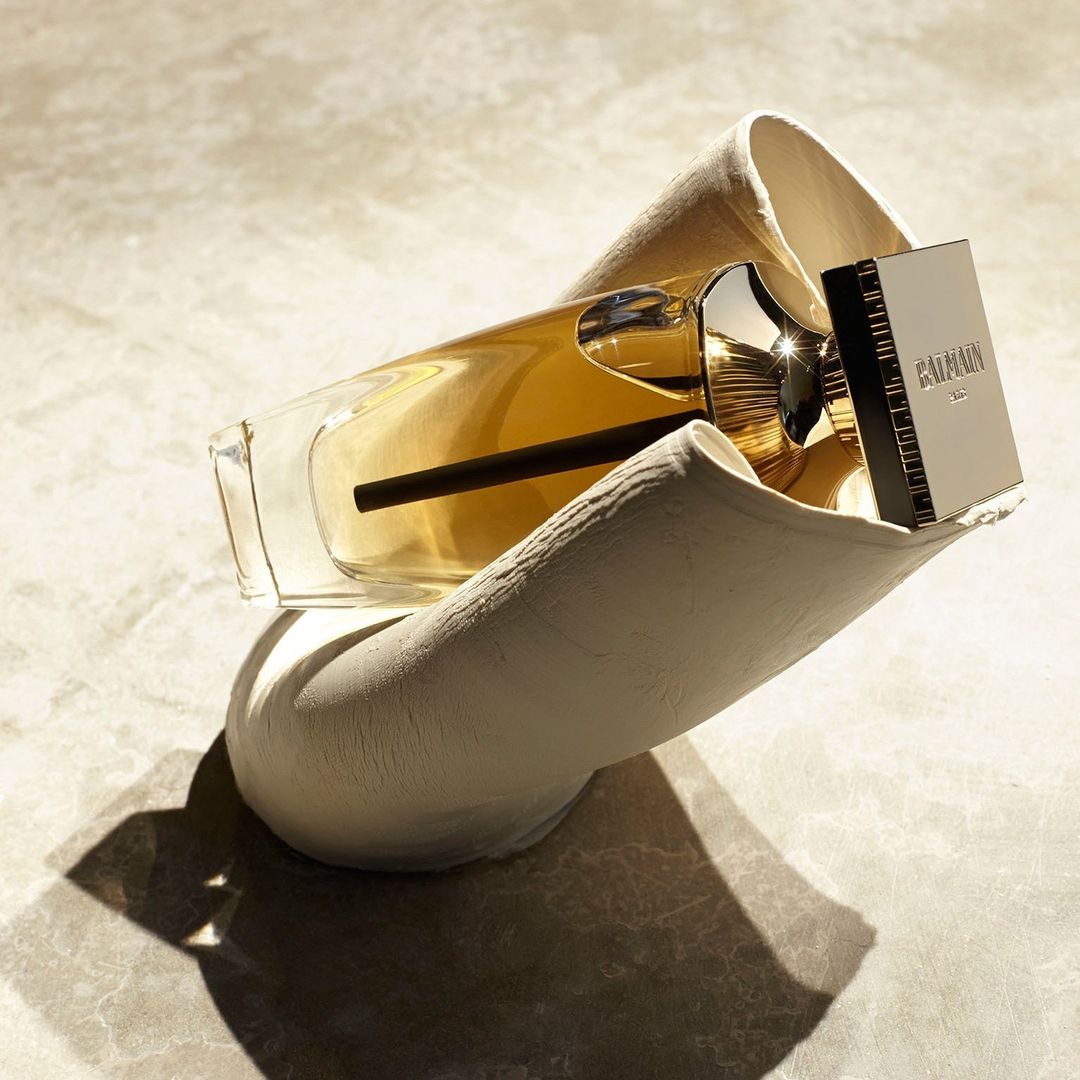 Balmain fragrance bottle resting inside a sculptural off-white textured holder under hard natural lighting