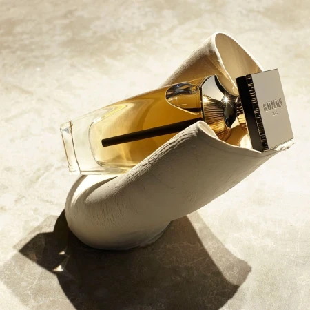 Balmain fragrance bottle resting inside a sculptural off-white textured holder under hard natural lighting