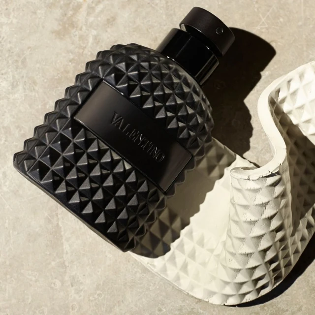Black Valentino perfume bottle with a textured, studded design on a gray stone surface with a white textured support.