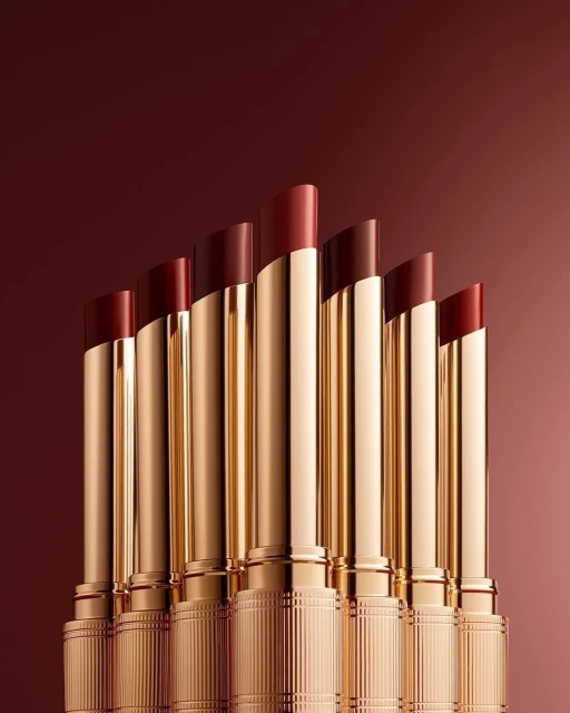 Seven shades of lipstick in a row with gold cases. The lipstick colors range from red to maroon, displayed on a gradient background.
