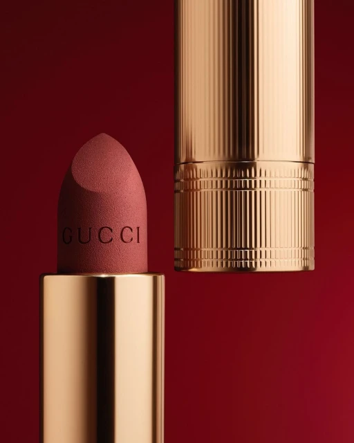 Close-up of a gold Gucci lipstick tube with the lipstick exposed against a solid red background in a beauty product shot.