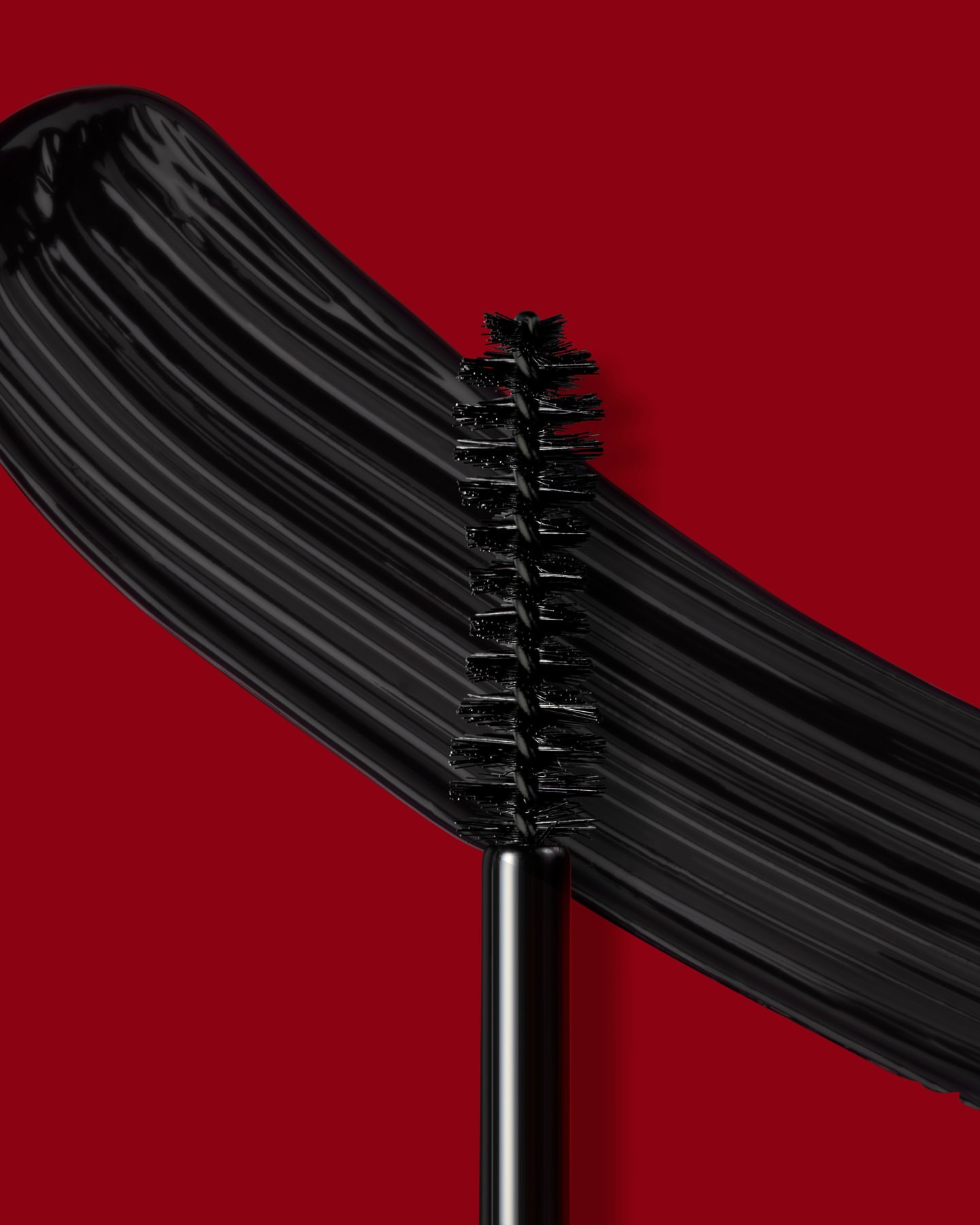 Macro studio shot of a mascara wand with thick black mascara swatch on a red backdrop, showcasing beauty and cosmetic application.