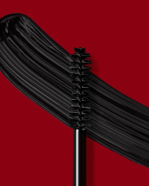 Macro studio shot of a mascara wand with thick black mascara swatch on a red backdrop, showcasing beauty and cosmetic application.