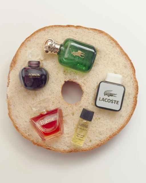 Several miniature perfume bottles from different brands sit atop a slice of bread with a hole in the middle, photographed from above.